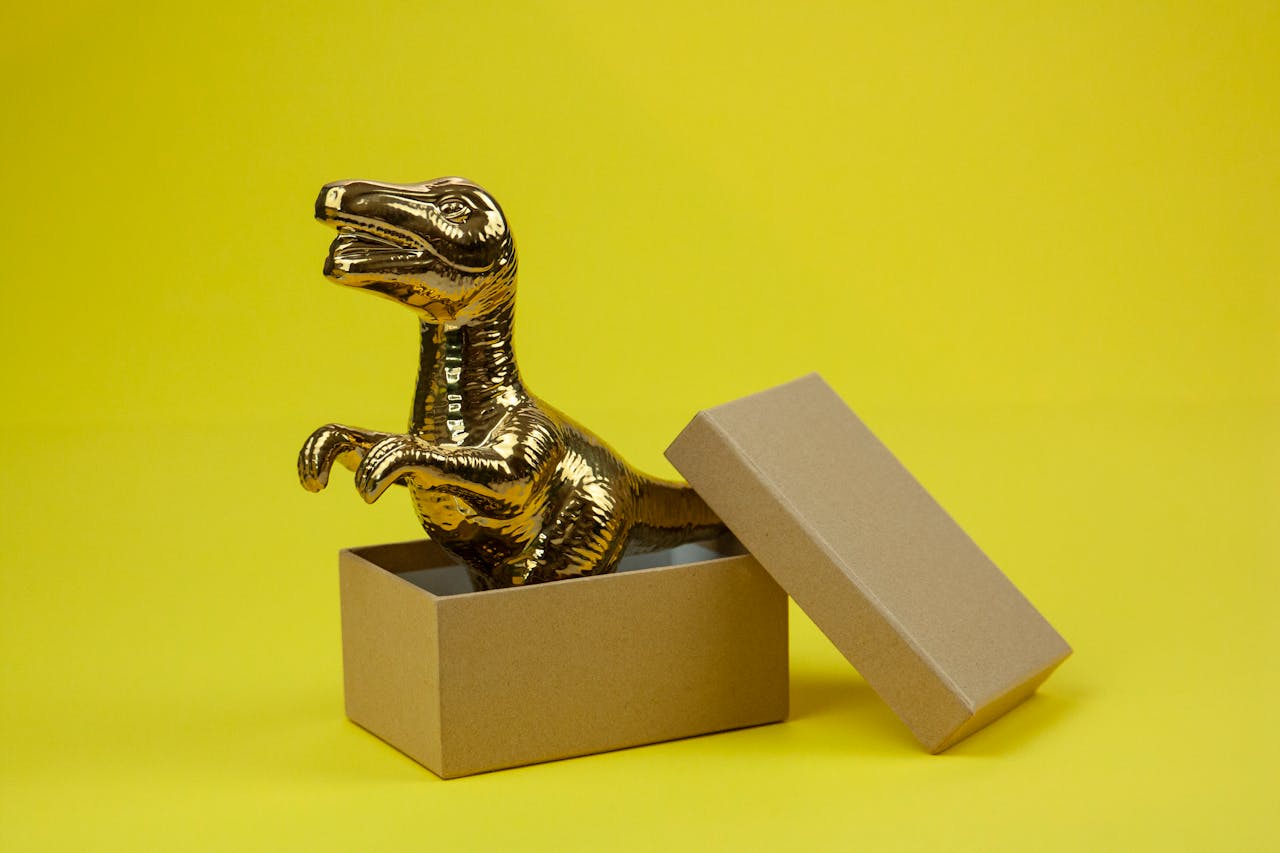 Golden dinosaur figurine emerging from a box against a bright yellow background, showcasing creativity and fun.